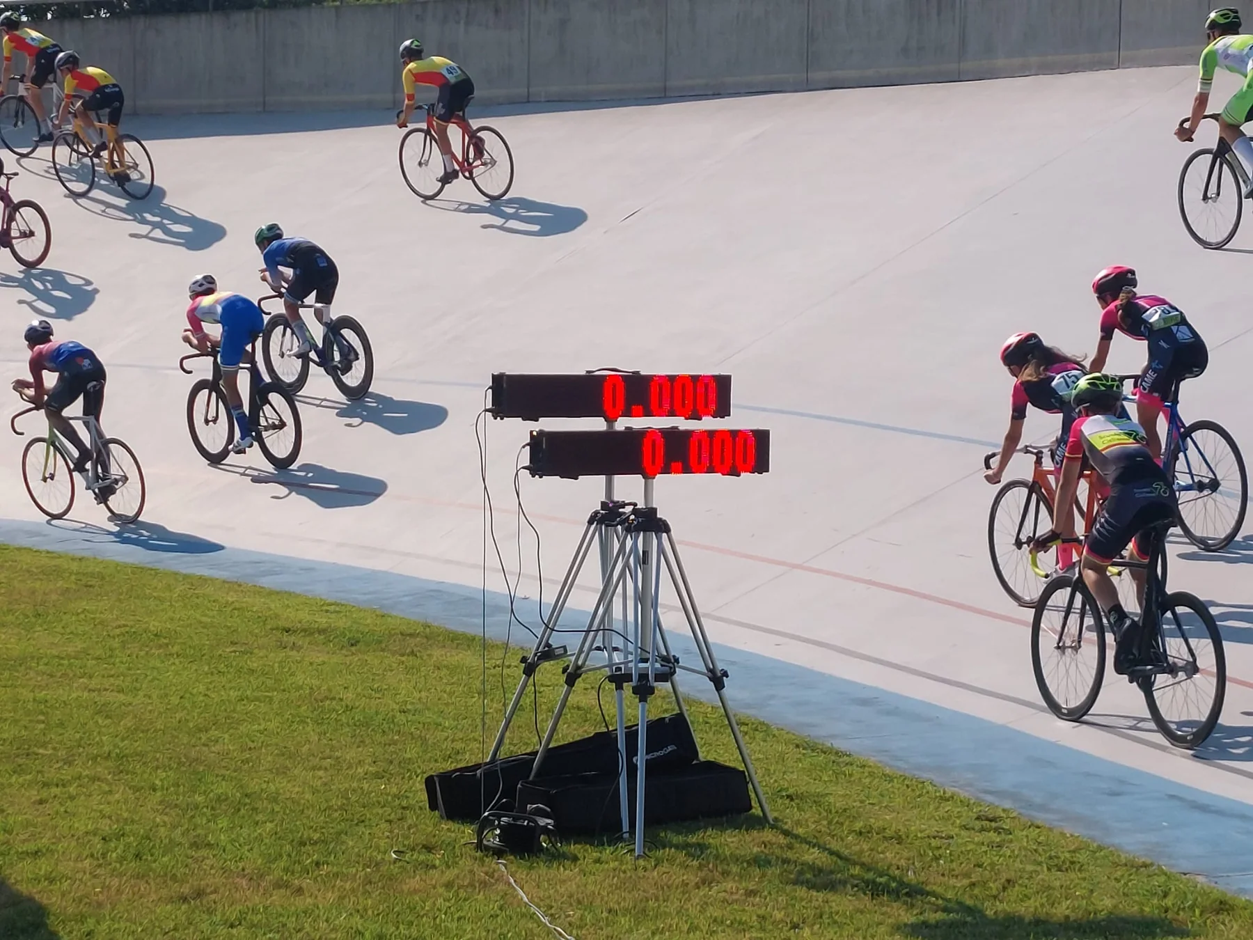 Ciclisti su pista durante una gara, con tabelloni elettronici per il cronometraggio a bordo pista.